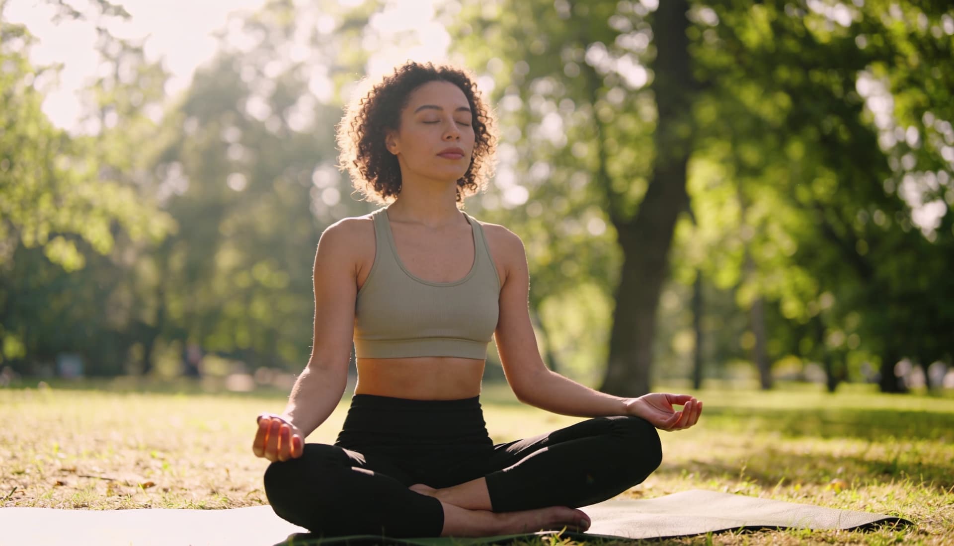 Woman meditating on a yoga mat in a sunlit park